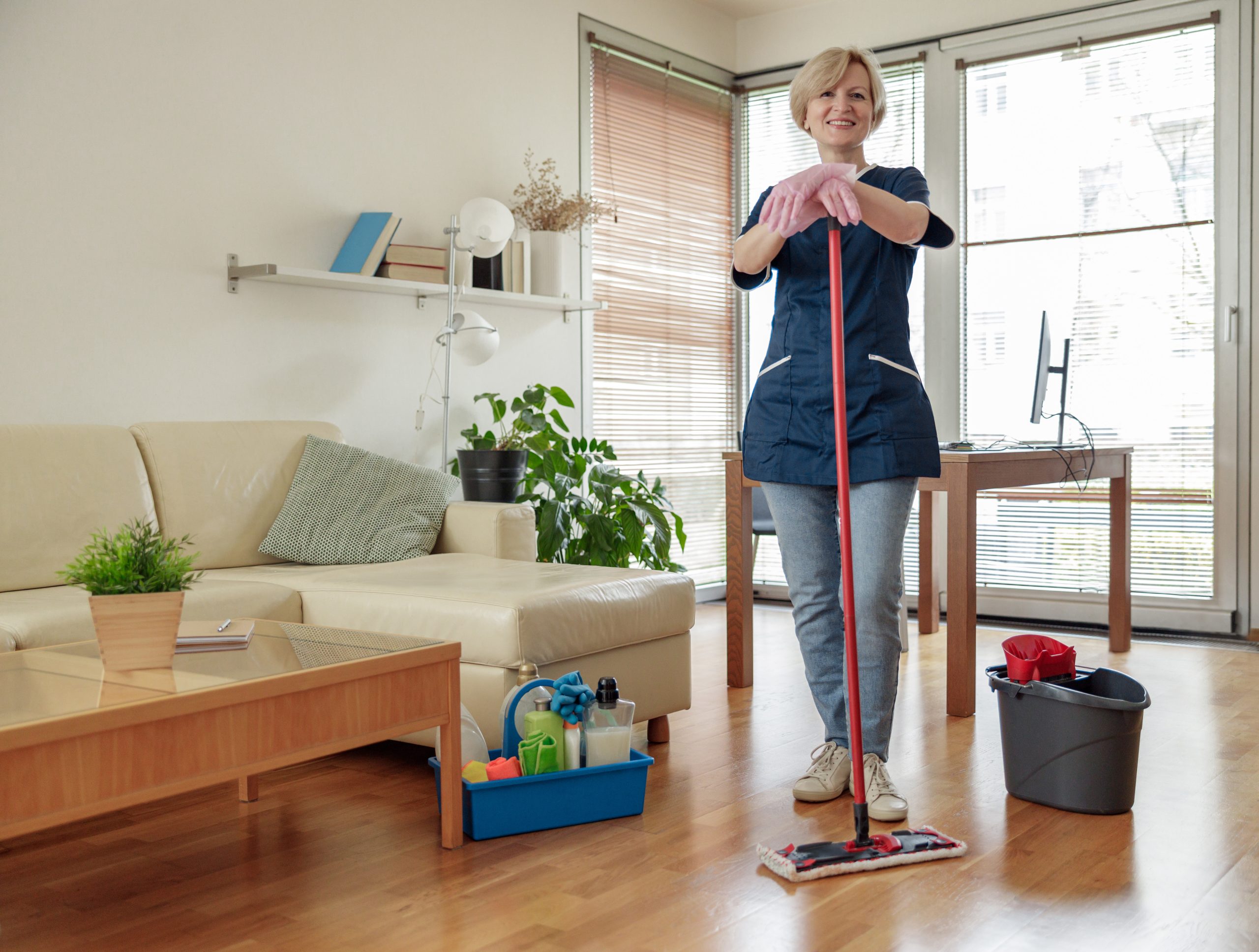 Professional smiling housemaid in uniform washing floor with mop in living room Apartment Cleaning Service Cost
